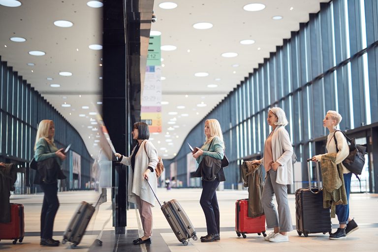 Horizontal side view shot of four women standing in queue with their luggage at airport check-in counter, copy space