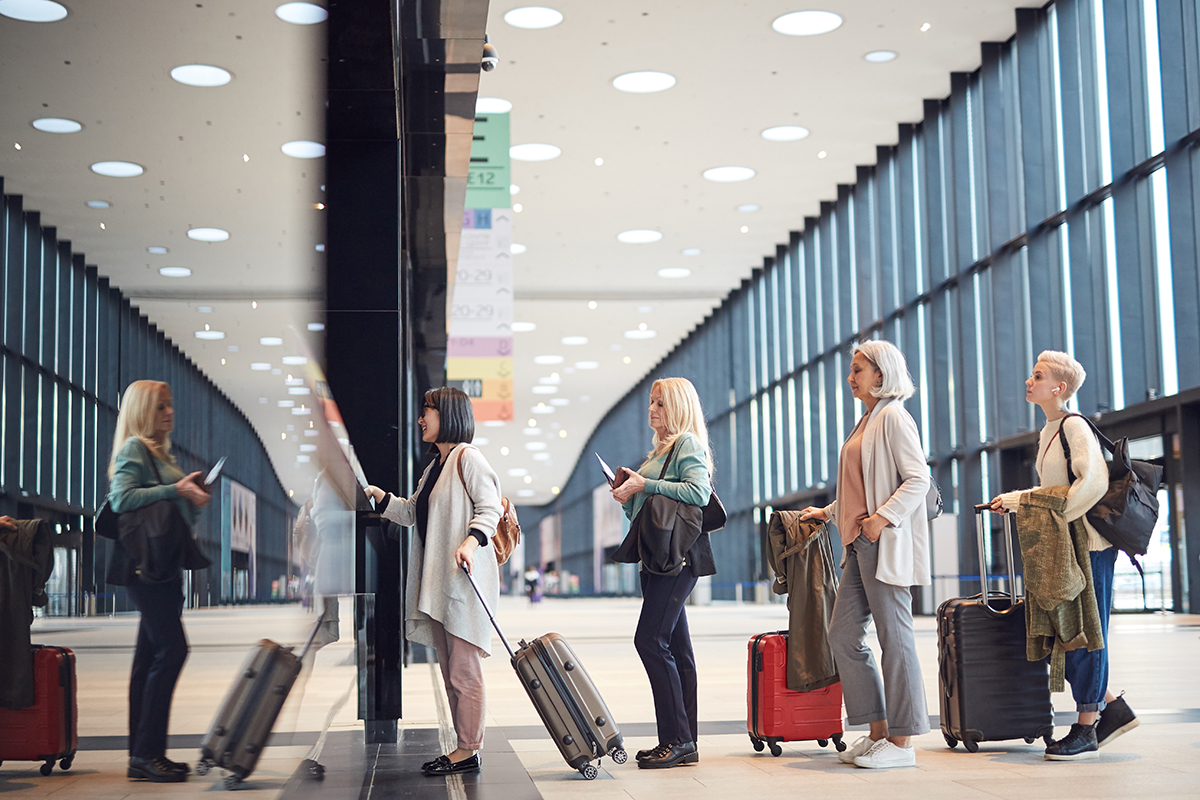 Horizontal side view shot of four women standing in queue with their luggage at airport check-in counter, copy space